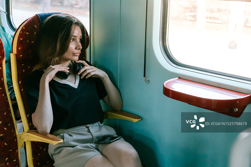 移动的旋律:一个女人沉浸在音乐中，手拿手机，坐在火车窗口图片素材