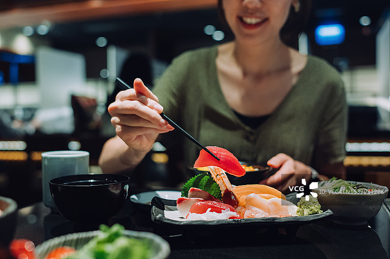 在一家日本餐厅里，年轻的亚洲女子微笑着享用着新鲜的生鱼片配味噌汤和绿茶。亚洲美食和饮食文化。人，食物和生活方式图片素材