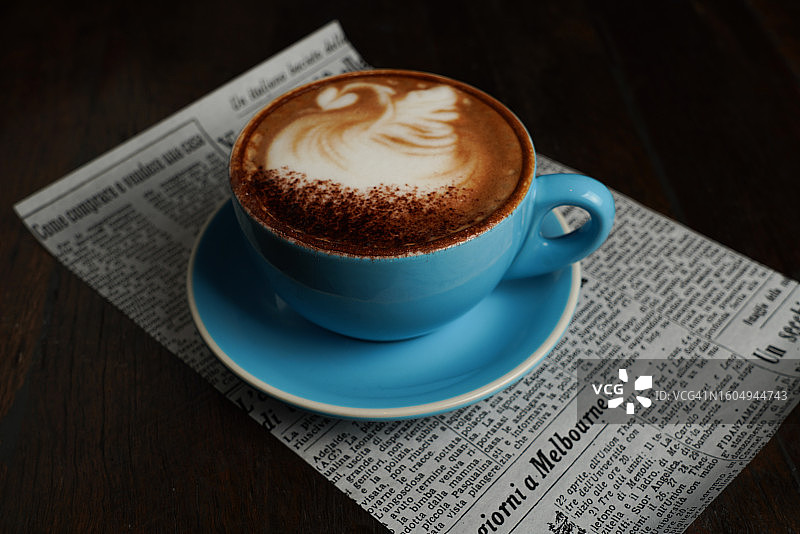 一杯蓝色杯子里的咖啡，放在一张报纸上图片素材