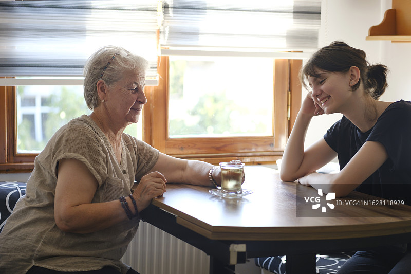 奶奶和孙女在厨房的桌子边喝茶聊天图片素材