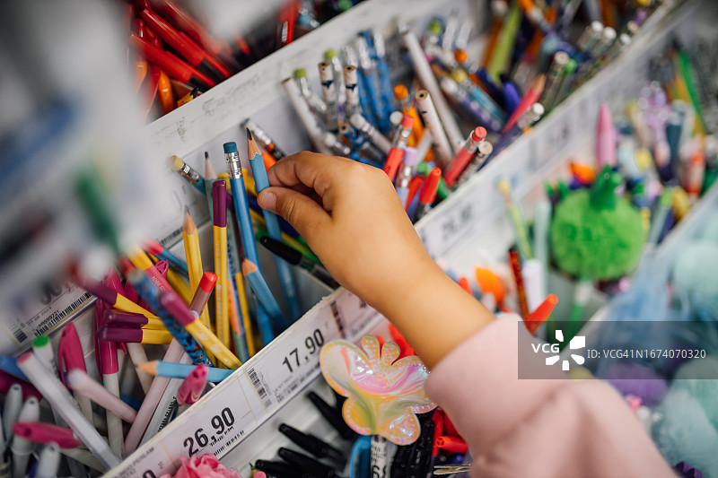 在书店的学习用品区，一个无法辨认的女孩正在挑选彩色钢笔和铅笔图片素材