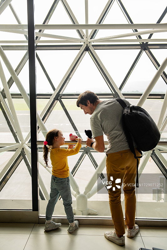 年轻的父亲和女儿在机场候机楼玩玩具，等待飞机起飞。图片素材