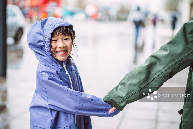 可爱开朗的女孩穿着雨衣和她的朋友一起走在一个雨天的城市街道图片素材