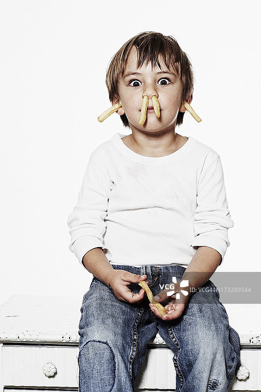 男孩的肖像(6-7岁)，鼻子和耳朵里插着薯条图片素材