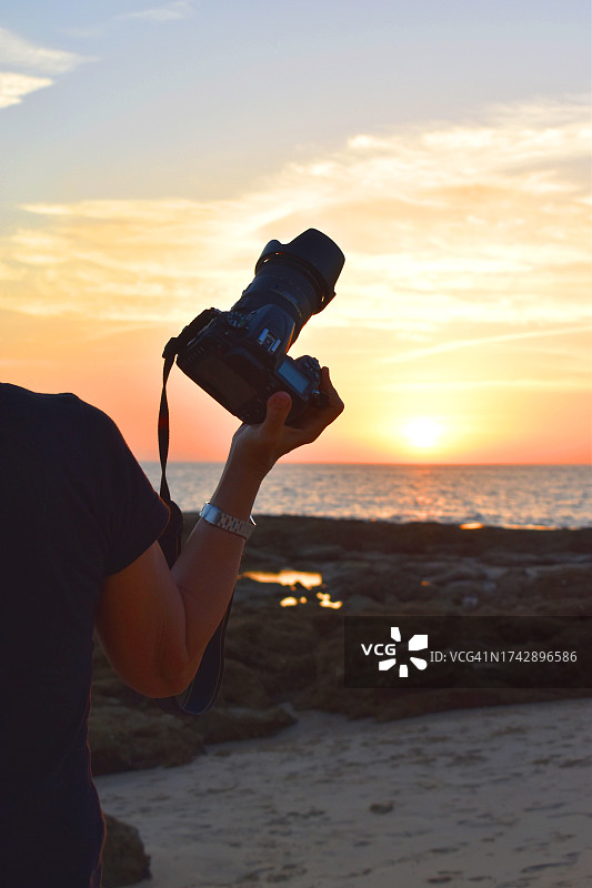夕阳下的沙滩上，手持相机的女性图片素材