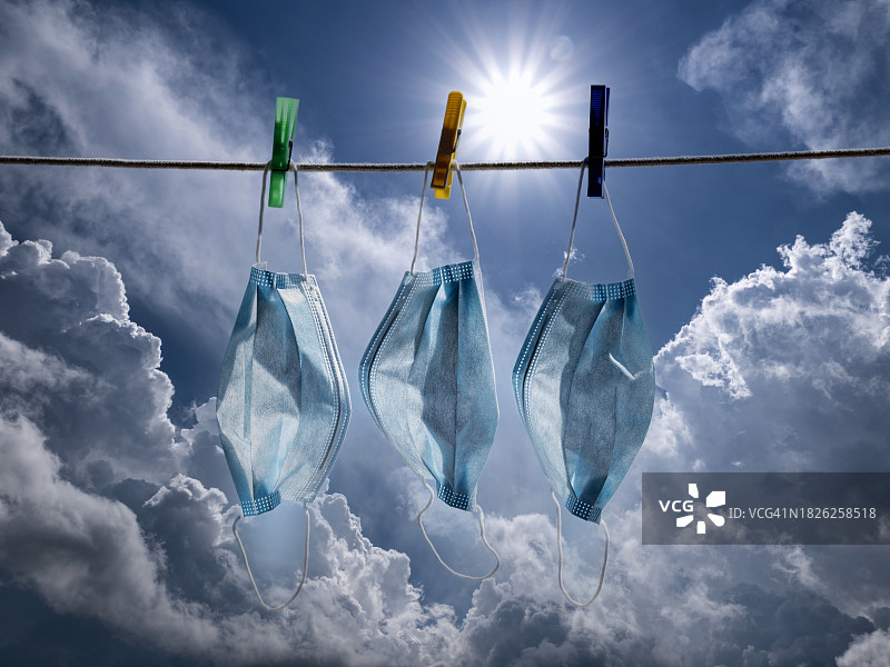 三个洗过的蓝色医用口罩挂在晒衣绳上，晒着阳光明媚的天空。图片素材
