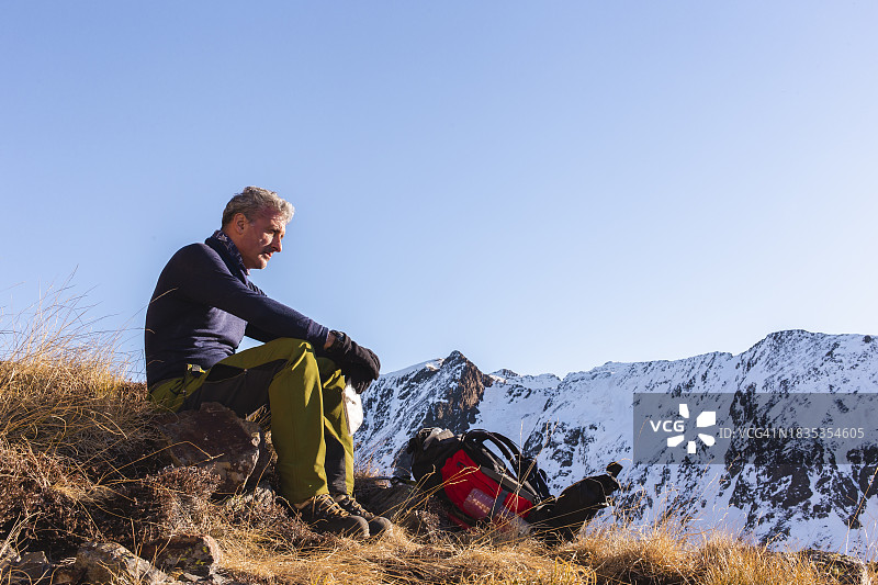 冬天，一个人背着背包坐在山上沉思图片素材