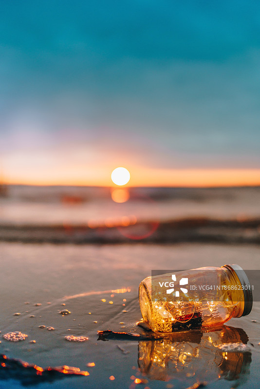 日落时，沙滩上的瓶子对着天空的特写图片素材