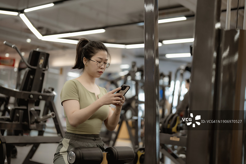 女性使用器械进行锻炼、休息，空闲时间使用智能手机图片素材