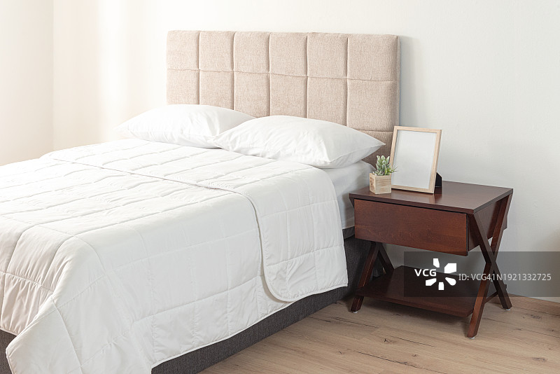 一个现代卧室的内部，有一张白色的床，上面有舒适的床单和一个木制的床头柜，还有一个米色的织物床头板图片素材