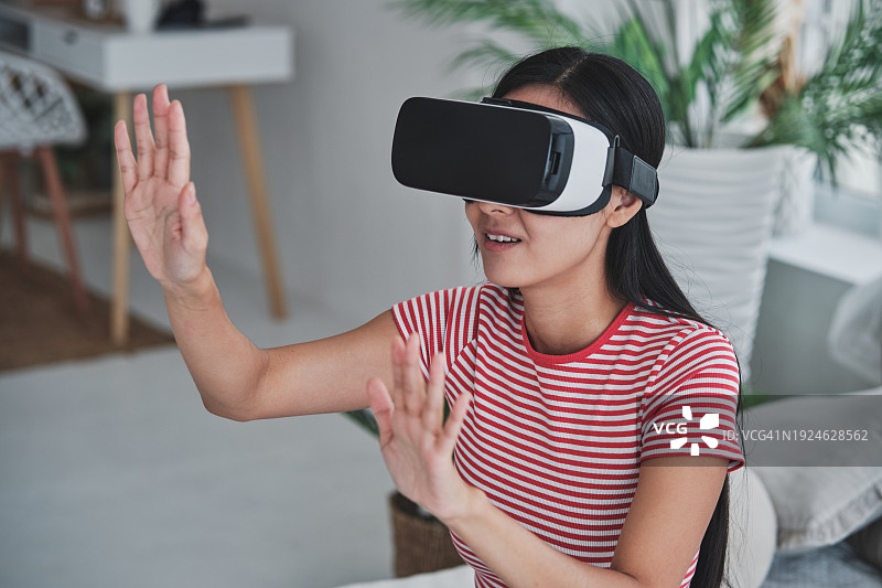 亚洲女性在家使用虚拟现实耳机，女孩戴着VR眼镜用手触摸空气，观看3d视频，在虚拟世界购物。人与创新的未来技术图片素材