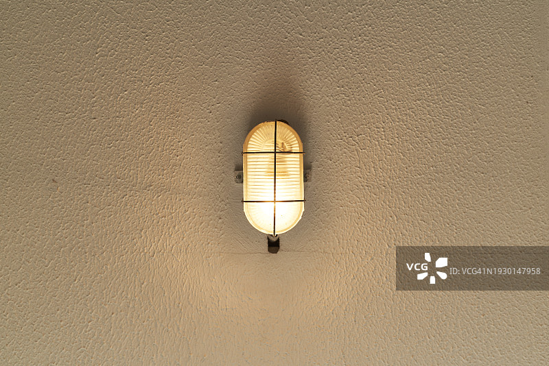 一盏小灯挂在质朴的奶油色墙壁上，周围有电线。图片素材