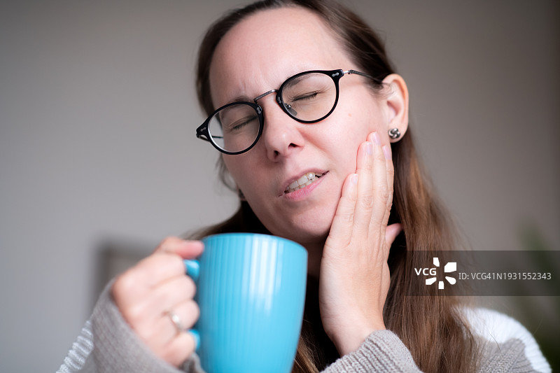 喝着热茶的女人正在遭受牙齿敏感的折磨图片素材