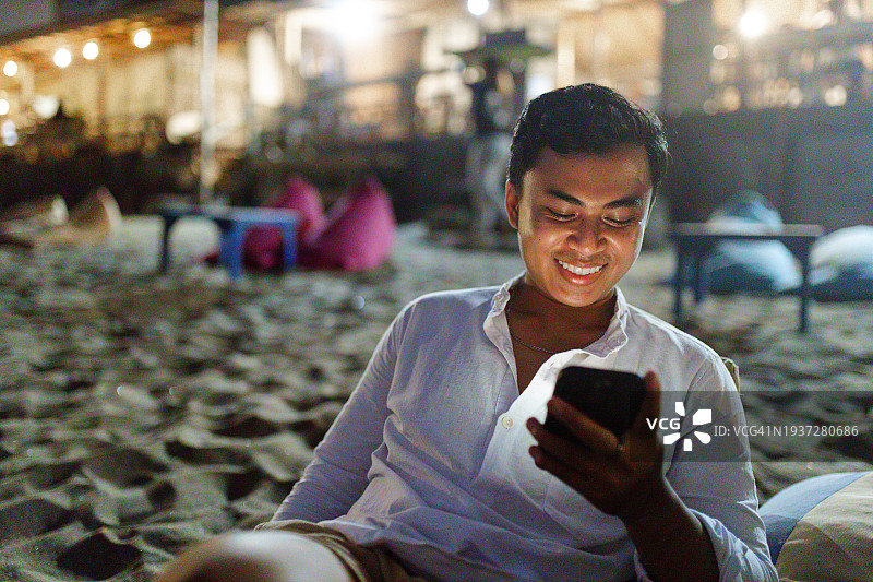 一个年轻人坐在沙滩上玩手机图片素材