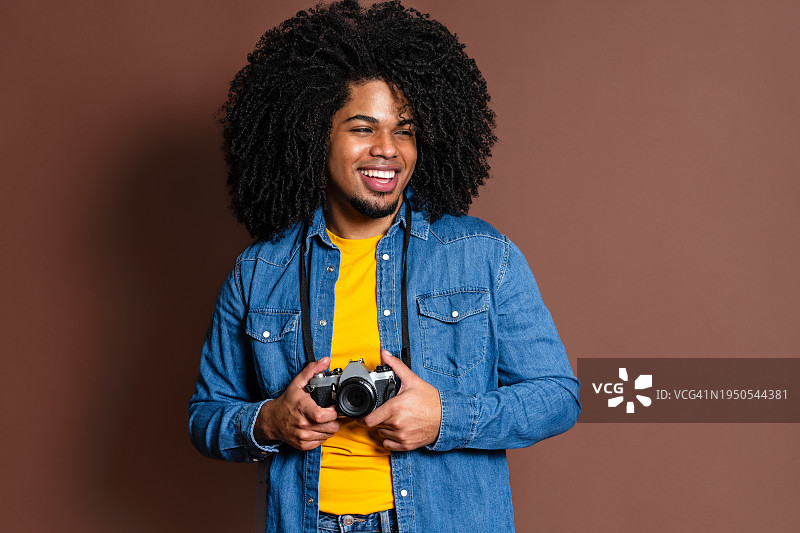 愉快的非洲头发的男人与相机在棕色背景图片素材