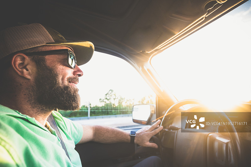 一个快乐的中年男人，戴着胡子墨镜和帽子，开着汽车或SUV，涂着防晒霜图片素材