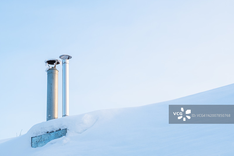 房屋屋顶上用于供暖的铝管，背景是天空和雪。在下雪的气候中为桑拿房和房屋供暖图片素材
