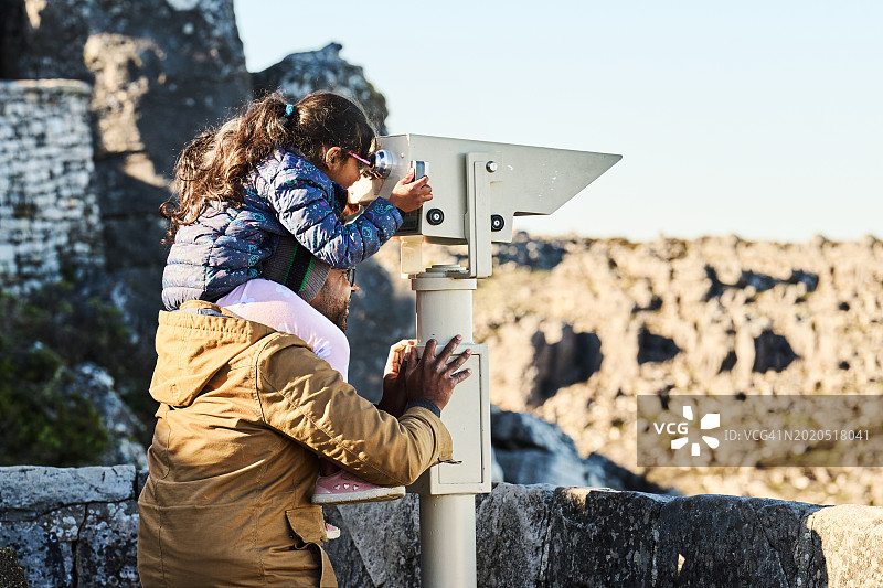 一家人在观测点通过固定的双筒望远镜观看山景图片素材