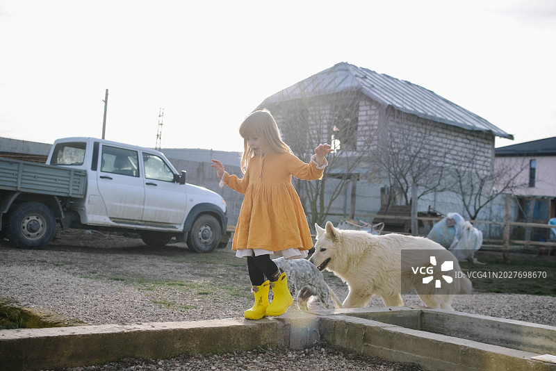 一个女孩牵着狗走在房子的院子里。图片素材
