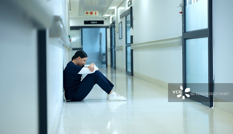 医生，女人和悲伤的地板在走廊上的抑郁，倦怠或悲伤的死亡在医院。医生，护士或人的压力，疲劳或担心在走廊，坐在或在诊所晚上疲劳图片素材