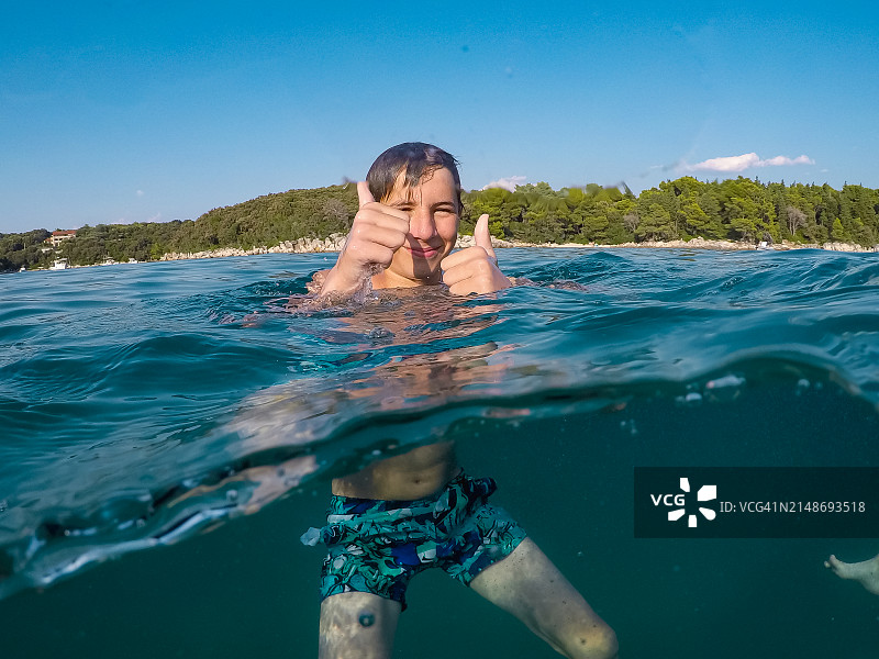 快乐的少年在海里竖起大拇指，用可穿戴式水下相机拍摄图片素材