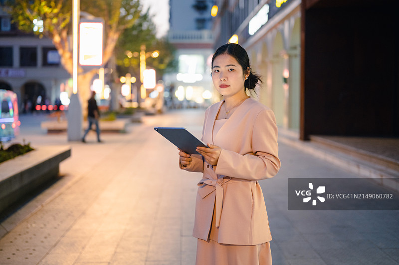 晚上，年轻的亚洲女商人手持iPad站在街上图片素材