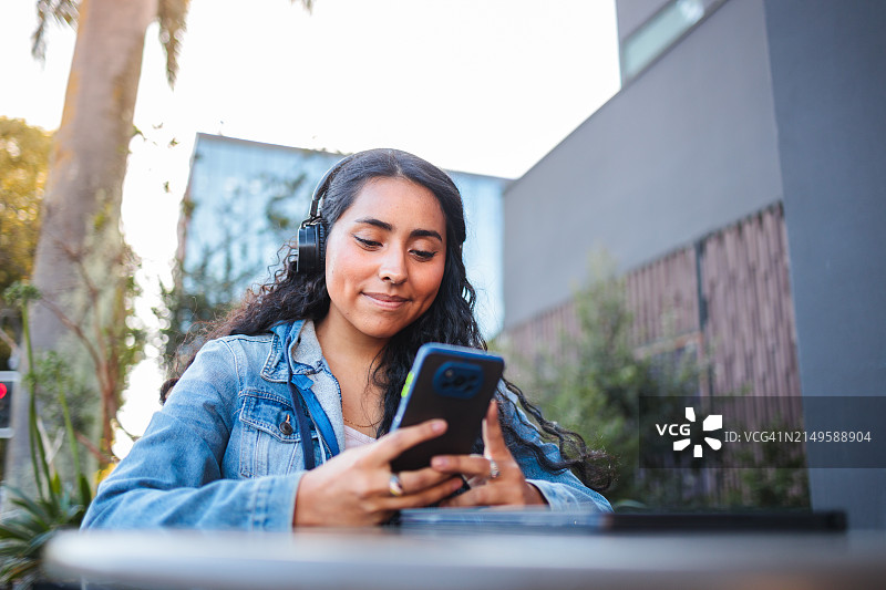 年轻的拉丁女性一边在户外咖啡馆放松，一边监控银行应用程序和数字投资图片素材
