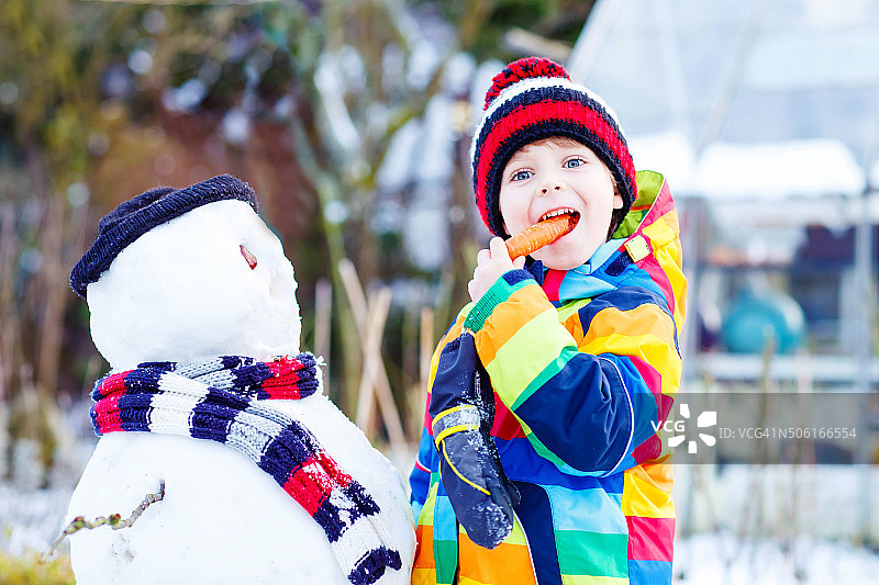 滑稽的小男孩穿着五颜六色的衣服在户外堆雪人图片素材