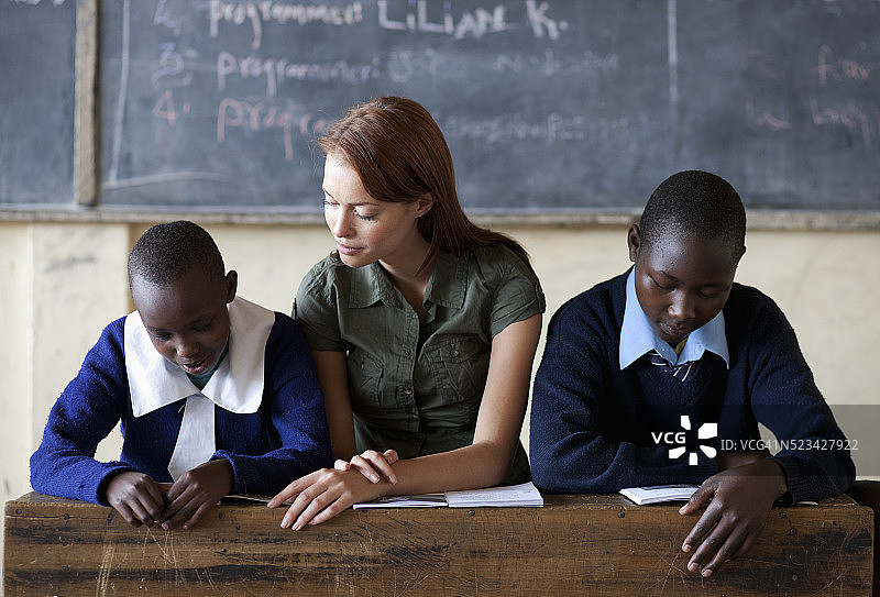肯尼亚，两名学生和老师坐在教室里看书图片素材