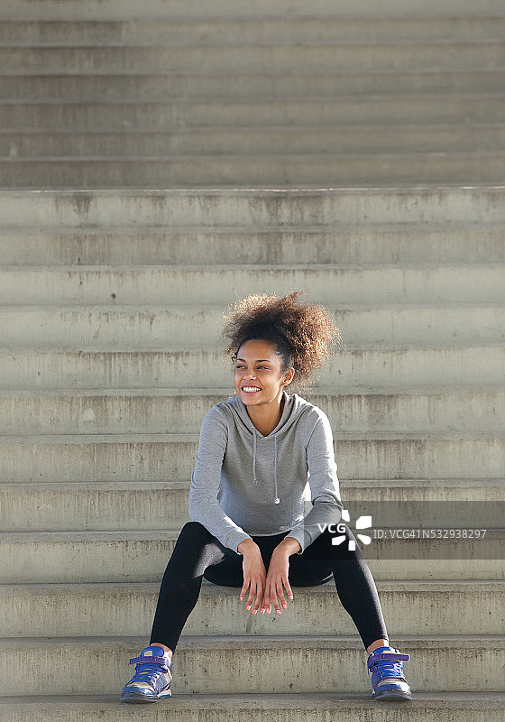 快乐的年轻女运动员坐在户外的台阶上图片素材