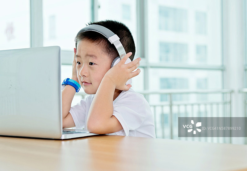 年轻的亚洲男孩戴着耳机使用笔记本电脑图片素材