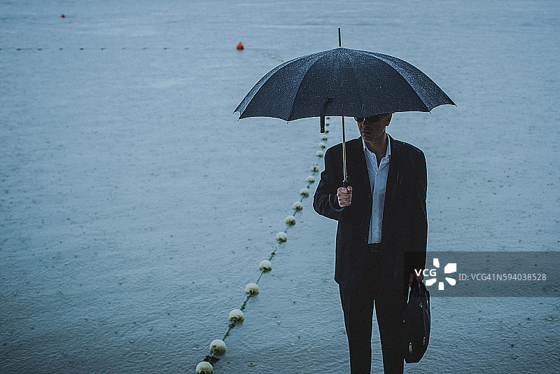 帅气的男人穿着西装，在雨中撑着伞图片素材