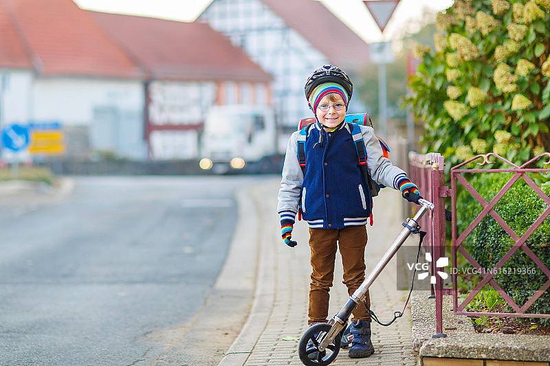 戴着头盔的小男孩骑着滑板车穿过城市图片素材
