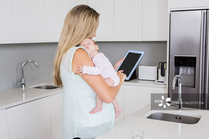 妈妈抱着孩子在厨房里玩平板电脑图片素材