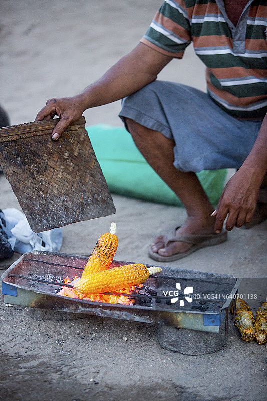 一个当地的小贩在海滩上卖玉米。图片素材