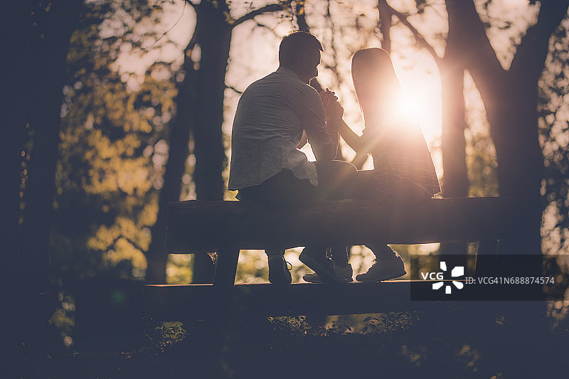 日落时分，一对年轻浪漫的情侣在长椅上聊天。图片素材
