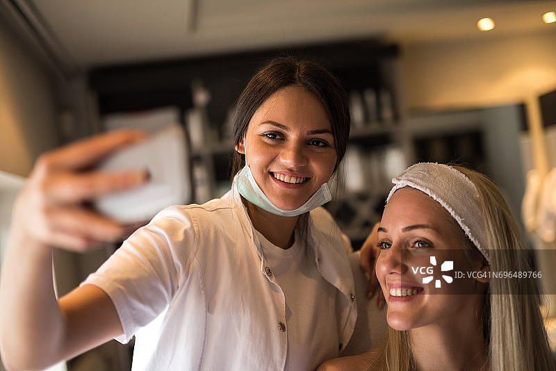 快乐的美容师与女性客户在沙龙自拍。图片素材