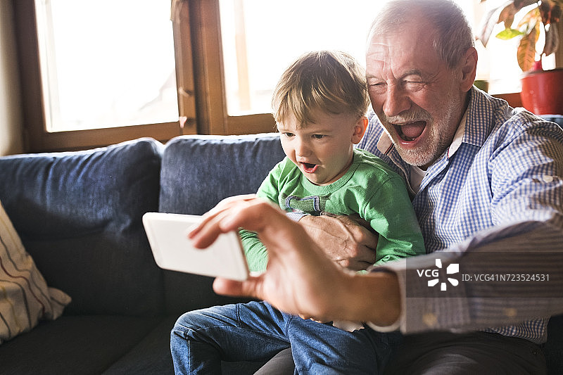 爷爷和孙子坐在沙发上，用智能手机自拍图片素材