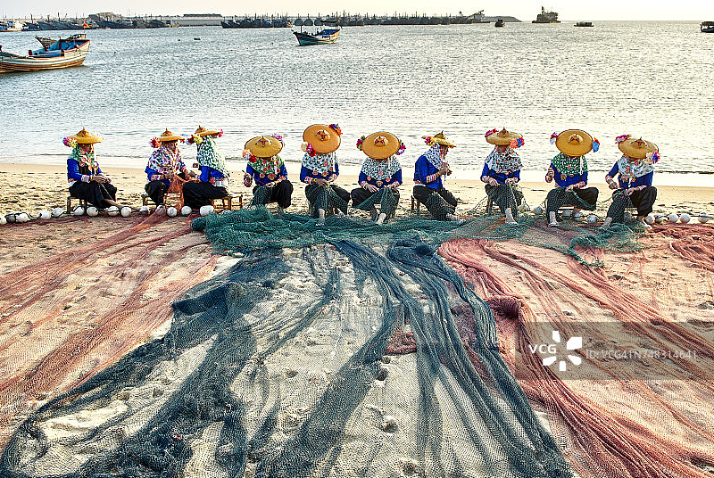 中国福建大佐，身穿传统服饰的渔民在海滩上修补渔网图片素材