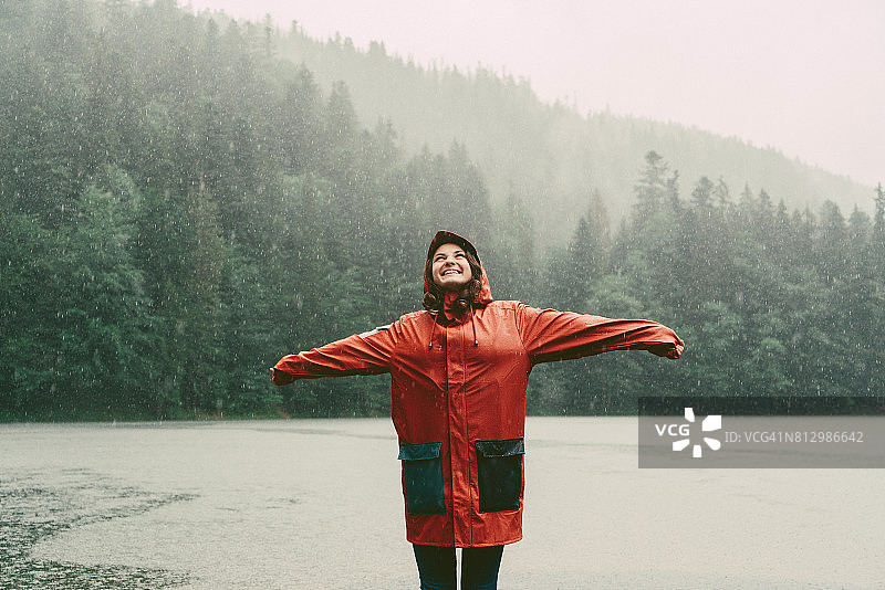 一个穿着雨衣的女人站在倾盆大雨下的湖边图片素材