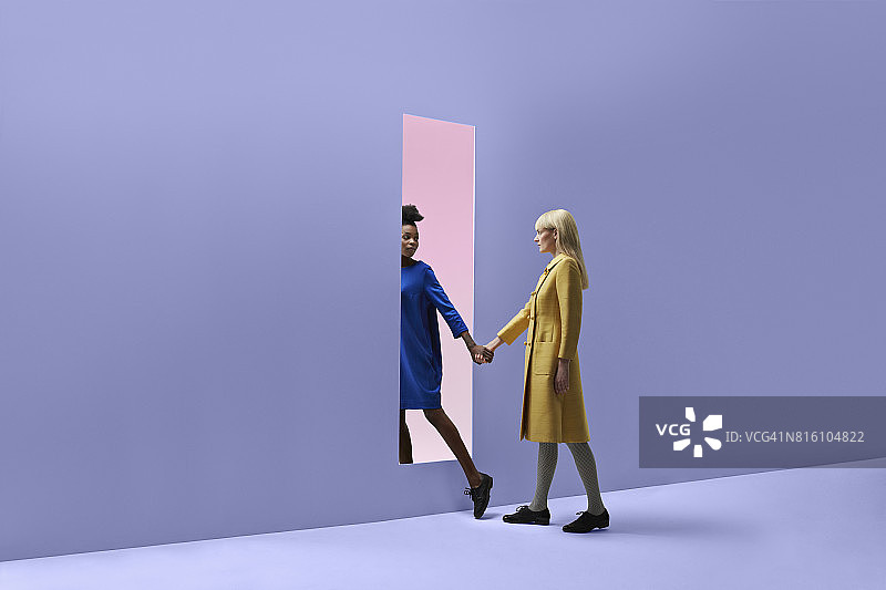 两个女人手牵着手，在彩色的墙上扔出一个长方形的口子图片素材