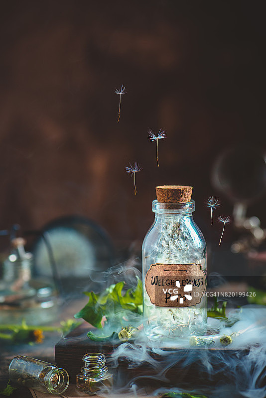 玻璃药水瓶蒲公英种子和手工制作的标签在一个神奇的静物与烟图片素材