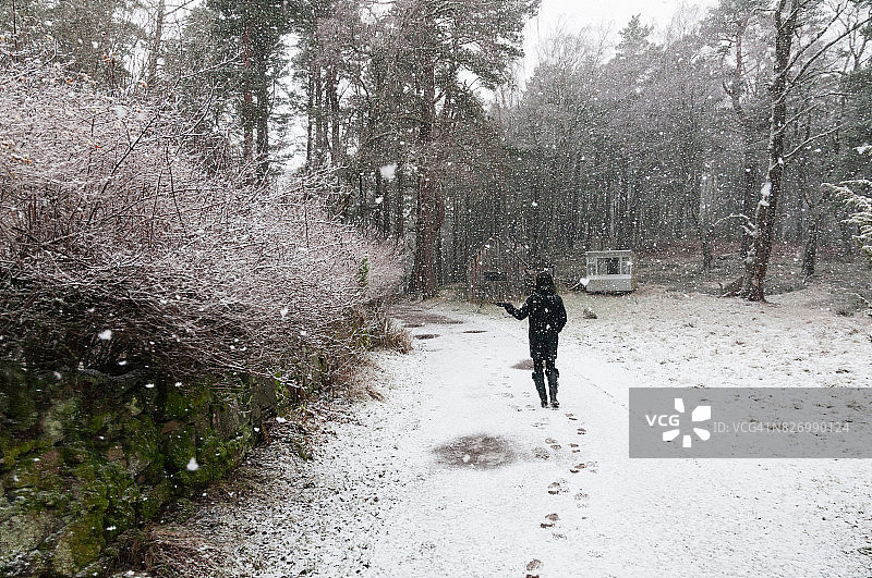 穿着黑色衣服的女孩走在雪地上，抓着雪花图片素材