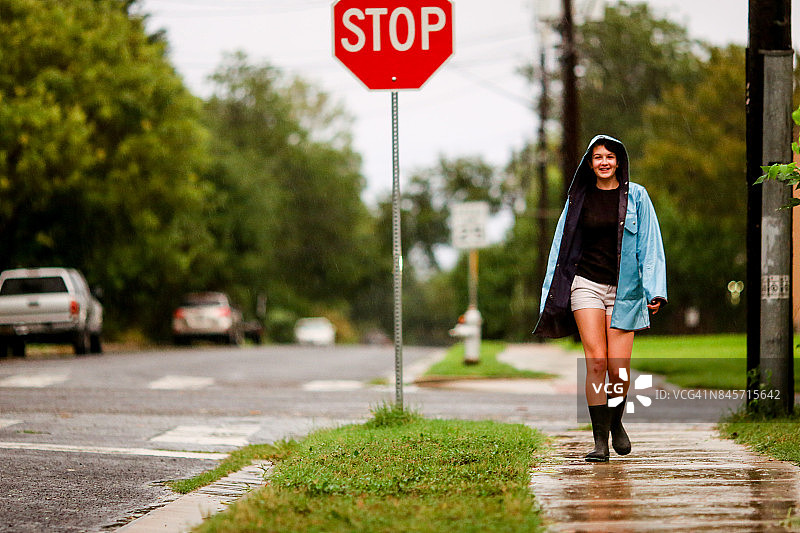 一个十几岁的女孩穿着蓝色雨衣在雨中的人行道上图片素材