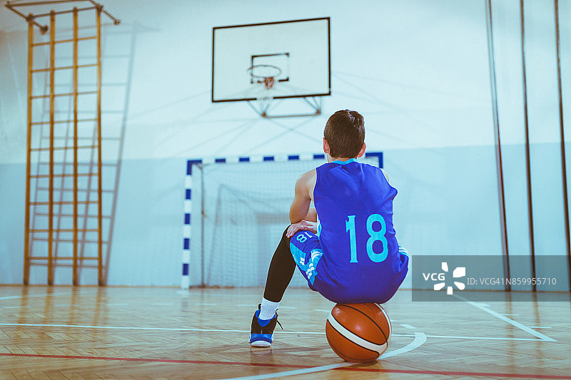 年轻的篮球运动员坐在操场上的球上图片素材