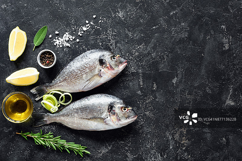 新鲜的鱼海鲷，香草，香料，橄榄油和烹饪原料在石板背景。图片素材