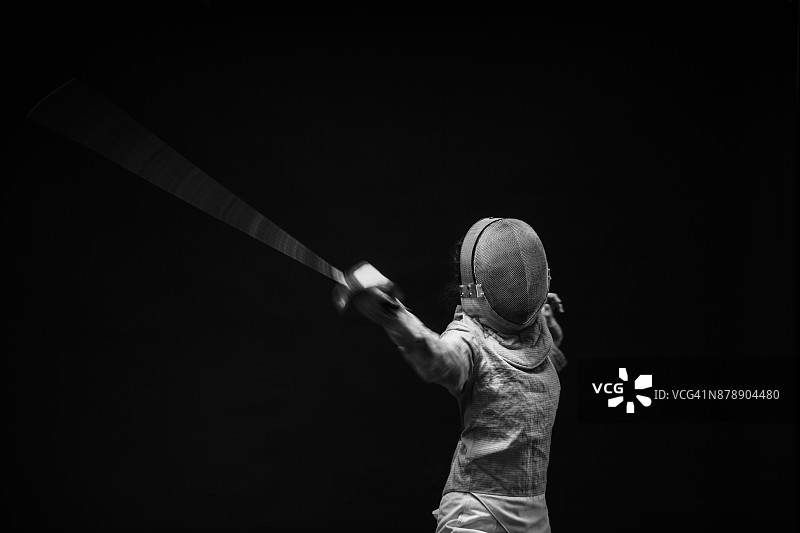 击剑运动在击剑姿势的年轻女子击剑动作。黑色背景。图片素材