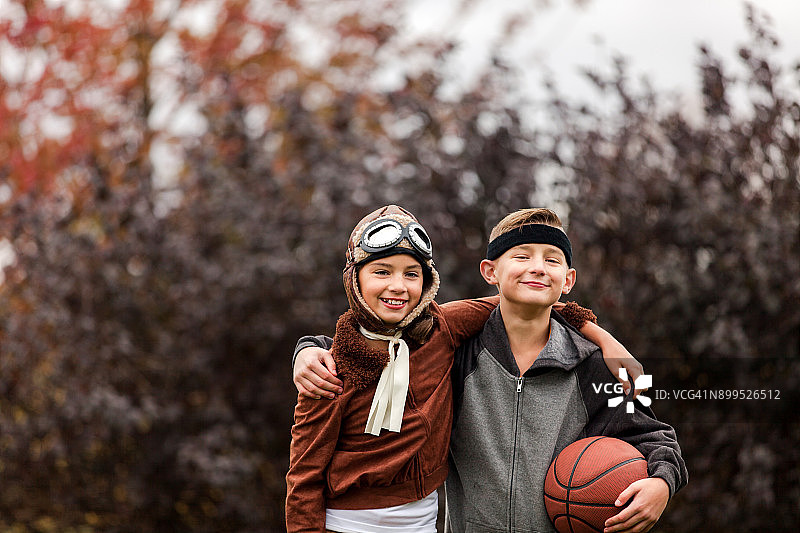 女孩和双胞胎兄弟的肖像穿着篮球运动员和飞行员的服装在公园万圣节图片素材