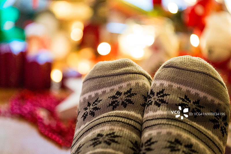 近距离的脚穿着温暖舒适的斯堪的纳维亚风格的圣诞袜下照明圣诞树图片素材
