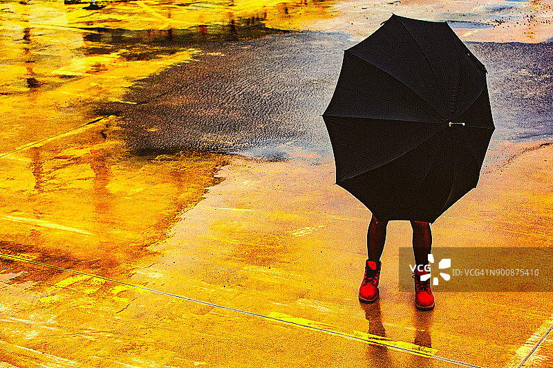 一名年轻女子撑着伞，站在寒冷、多风、多雨的秋日的户外。图片素材